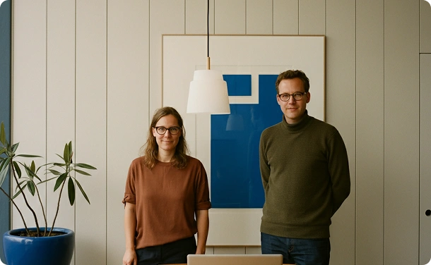 mannen en vrouwen die in een modern kantoor staan Dit is een foto van twee volwassen mannen en een vrouw die in een modern kantoor of een werkruimte staan. De inrichting is minimalistisch, met lichte muren, verticale panelen en een eenvoudig, strak interieur. Achter hen hangt aan de muur een groot abstract schilderij waarin de kleur blauw overheerst. In het midden van de compositie hangt een witte lamp met een licht gebogen en brede lampenkap, die een zacht licht verspreidt.